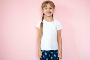 jolie peu fille dans une blanc T-shirt souriant sur une rose Contexte photo