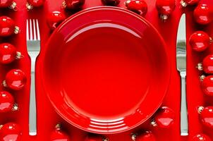 rouge assiette avec couteau et fourchette avec rouge babioles sur rouge Contexte pour Noël vacances à manger concept. photo