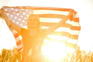 magnifique Jeune fille en portant un américain drapeau dans le vent dans une champ de seigle. été paysage contre le bleu ciel. horizontal orientation. photo