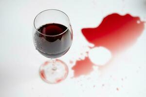 rouge du vin dans une transparent verre et déversé boisson sur une blanc Contexte photo