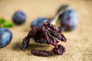 séché pruneaux dans une cuillère sur une toile de jute nappe de table contre une Contexte de Frais prunes. photo