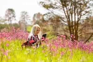 femme travail sur tablette en ligne dans été parc sur herbe. femme la personne affaires la nature à l'extérieur avec en ligne technologie. électronique gadgets distance apprentissage concept. photo