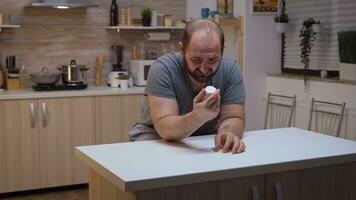 épuisé homme en portant une bouteille de pilules séance dans le cuisine. stressé, fatigué malheureux inquiet indisposé la personne Souffrance de migraine, dépression, maladie et anxiété sentiment mauvais avec vertiges symptômes photo