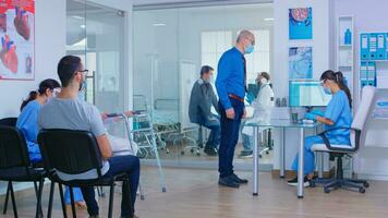 Sénior homme avec visage masque contre covid19 à hôpital accueil parlant avec infirmière. médecin avec patient dans examen chambre. désactivée mature femme avec en marchant Cadre dans attendre zone. photo