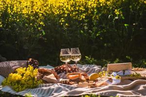 pique-niquer au coucher du soleil au champ de colza verre de vin bun alimentaire photo