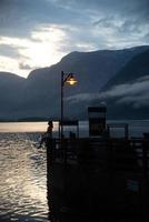 Femme à l'ancienne jetée en bois regardant le coucher du soleil sur le lac de la mer de Hallstatt photo