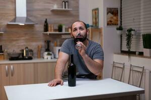 pensif homme en buvant verre de du vin tandis que séance seul et déprimé. la personne avec de l'alcool dépendance ayant bouteille de alcoolique boisson, alcool, biberonner, sentiment navré et désespéré photo