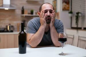 désespéré homme sentiment misérable tandis que ayant verre avec du vin et bouteille en buvant seule. la personne avec mauvais pour la santé dépendance séance avec alcool, biberonner, alcoolique boisson étant dérangé photo