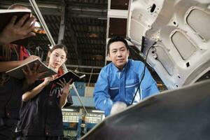 asiatique Masculin professionnel automobile ingénieur superviseur décrit voiture moteur entretien et réparation travail avec mécanicien ouvrier états-majors équipe dans réparer un service garage, spécialiste métiers dans auto industrie. photo