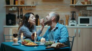 de bonne humeur couple dépenses soumissionner moment à dîner. épouse et mari pendant romantique repas dans cuisine, à manger ensemble à maison, profiter célébrer leur anniversaire, surprise vacances à bougie lumières photo