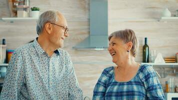 Sénior couple en riant tandis que à la recherche à caméra dans cuisine. de bonne humeur vieux homme et femme souriant et en riant. content personnes âgées retraité les personnes dans confortable Accueil profiter la vie photo