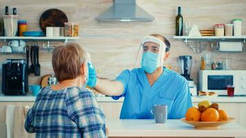 médecin avec visage masque vérification Sénior femme Température en utilisant pistolet thermomètre pendant Accueil visite. social ouvrier visite vulnérable les personnes pour maladie diffusion la prévention pendant covid19 campagne photo