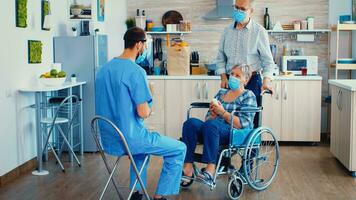 handicapé Sénior femme dans fauteuil roulant portant visage masque discuter avec médecin à propos traitement. social ouvrier offre pilules à handicapé personnes âgées femme. gériatre portion prévenir covid19 propager photo