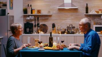 Sénior couple se détendre en mangeant dîner et en buvant du vin des lunettes ensemble dans le cuisine à Accueil ayant une romantique dîner. retraite couple célébrer leur anniversaire dans le à manger chambre. photo