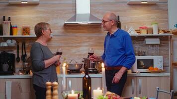 mari et épouse discuter à propos marrant des choses après romantique dîner. Sénior vieux couple en buvant du vin et en parlant, séance près cuisine tableau, célébrer leur anniversaire dans le à manger chambre. photo