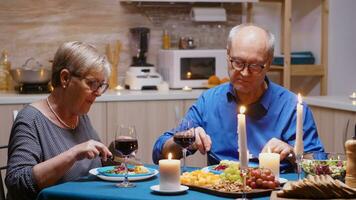 de bonne humeur vieux retraité couple dans l'amour ayant repas à maison. vieilli mature couple en mangeant et discuter pendant romantique dîner séance à le table dans le moderne cuisine, profiter temps ensemble photo