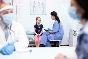 infirmière avec protection masque l'écriture enfant Les données sur presse-papiers pendant COVID-19 [feminine. santé médecin spécialiste fournir santé se soucier prestations de service consultations traitement dans protecteur équipement. photo