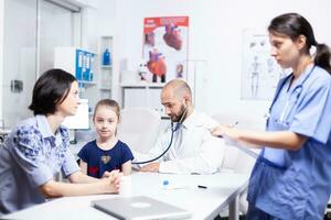 pédiatre écoute enfant souffle en utilisant stéthoscope pendant médical consultation. soins de santé médecin spécialiste dans médicament fournir santé se soucier prestations de service traitement examen. photo