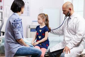 praticien médecin écoute enfant souffle avec stéthoscope dans hôpital clinique. spécialiste pédiatre dans médicament parlant à propos traitement maladie fournir soins de santé prestations de service photo