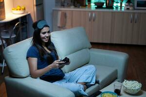 joueur en utilisant manette en jouant vidéo Jeux sur console séance sur canapé dans vivant chambre. excité déterminé femme en utilisant manette manette de jeu clavier playstation jeu et ayant amusement gagnant électronique Jeu photo