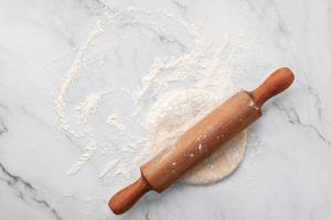 farine de blé dispersée et pâte à levure fraîche maison pétrie sur une table en marbre avec un rouleau à pâtisserie sur une table en marbre à plat.