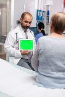 médical praticien avec vert écran tablette dans privé clinique pendant consultation de mature patient. prêt chrominance maquette pour votre application, texte, vidéo ou autre numérique actif. photo