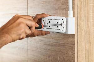 l'électricien utilise un tournevis pour installer la prise de courant électrique dans une boîte de sortie en plastique sur un mur en bois. photo