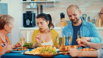élargi famille interagir tandis que ayant une repas à à manger table dans le cuisine. multi génération, quatre personnes, deux content des couples parlant et en mangeant pendant une gourmet dîner, profiter temps à maison. photo