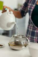 Dame fabrication chaud thé en utilisant Naturel herbes à profiter petit déjeuner dans cuisine. femme, style de vie, boisson, préparation, à base de plantes, théière, matin, aromatique. photo