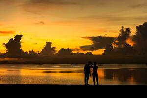 silhouettes gens tournage le le coucher du soleil à le lac. photo