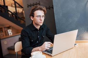 designer homme créatif travaillant sur son ordinateur portable en attendant les commandes dans son café préféré à l'intérieur, étudiant masculin travaillant sur net-book pendant le petit-déjeuner du matin dans l'intérieur d'un café moderne photo