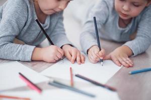 les enfants sont allongés par terre en pyjama et dessinent avec des crayons. enfant mignon peinture par crayons.main d'enfant fille et garçon dessiner et peindre avec un crayon. vue rapprochée photo