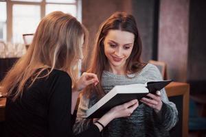 deux filles absorbées par la lecture d'un livre pendant la pause au café. jolies jeunes femmes lisent un livre et boivent du café photo