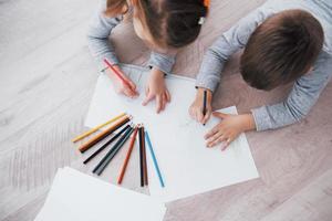 les enfants sont allongés par terre en pyjama et dessinent avec des crayons. peinture d'enfant mignon par des crayons photo