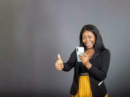 Jeune noir africain femme en portant mobile téléphone donné cogner en haut pour accord signe avec Succès affaires concept. photo