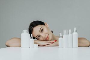 magnifique visage de Jeune caucasien femme avec parfait en bonne santé peau proposer une produit. fille avec shampooing, savon et crèmes maquette sur une blanc Contexte. gestes pour publicité. photo