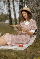 une Jeune magnifique femme dans une robe et une rond chapeau lit une livre photo