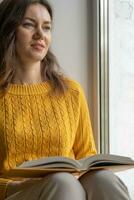 Jeune magnifique femme près fenêtre Jaune tricoté chandail lis livre photo
