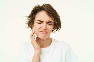 proche en haut de femme a une mal aux dents, touche sa les dents et fronce les sourcils de douloureux inconfort, des stands plus de blanc Contexte photo