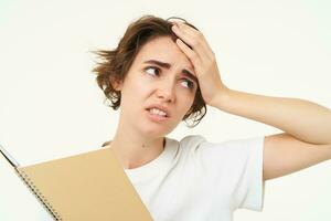 portrait de perplexe, dérangé Jeune femme fatigué de Faire devoirs, en portant planificateur avec compliqué affronter, permanent plus de blanc Contexte photo