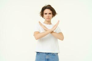 portrait de femme avec sérieux affronter, spectacles croix, Arrêtez geste, interdire quelque chose mauvais, permanent plus de blanc Contexte photo