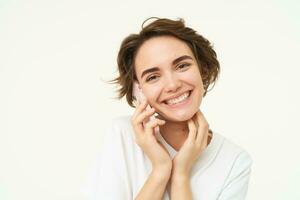 image de souriant, brunette femme appel quelqu'un, parlant sur mobile téléphone, répondre Téléphone appel, permanent plus de blanc Contexte photo