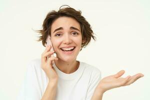 image de souriant, brunette femme appel quelqu'un, parlant sur mobile téléphone, répondre Téléphone appel, permanent plus de blanc Contexte photo