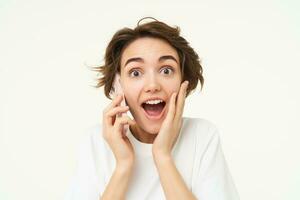 portrait de femme avec surpris affronter, réponses téléphone appel et regards excité, étonné par gros nouvelles, des stands plus de blanc Contexte photo