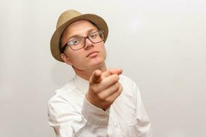 Jeune gars dans des lunettes et chapeau points une doigt à le caméra. photo