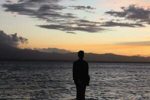 silhouette d'un jeune homme debout au bord du lac en profitant du coucher de soleil. atmosphère paisible dans la nature photo