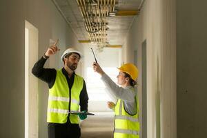 Masculin et femelle ingénieurs travail sur construction placer, elles ou ils sont surveillance le bâtiments électrique système. photo