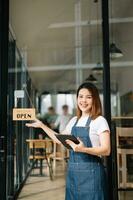 femme café magasin propriétaire en portant bloc-notes et numérique tablette prêt à recevoir ordres dans café restaurant. photo