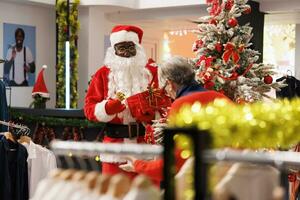 Père Noël claus homme dans costume en portant tombola à achats centre, attrayant personnes âgées la personne à participer à concours à gagner gratuit Vêtements article pendant Noël vacances saison. de fête décoré vente au détail magasin. photo