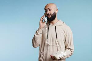 excité Jeune arabe homme en portant ligne fixe téléphone et ayant communication. émotif chauve barbu la personne répondre rétro Téléphone appel et parlant avec joyeux faciale expression photo